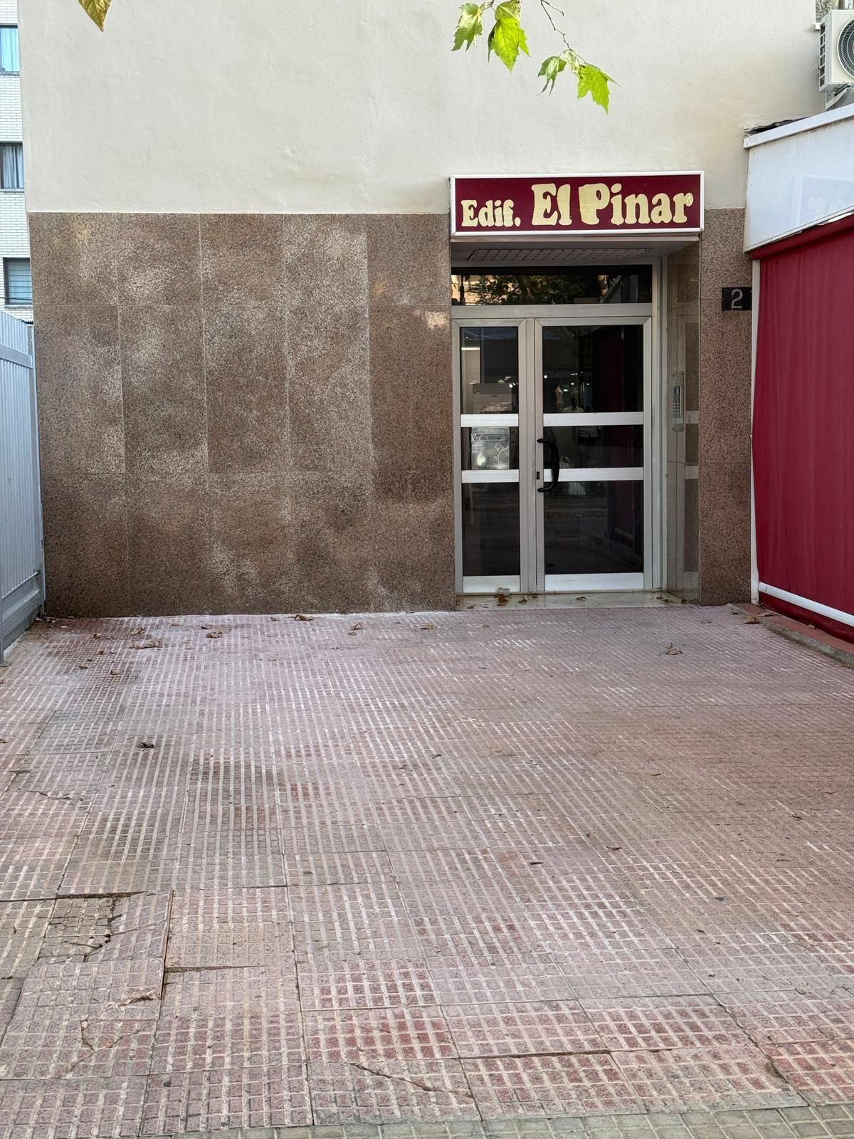 Une entrée d’immeuble avec une pancarte indiquant « Edif. El Pinar » et une porte rouge.