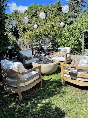 An outdoor seating area with wooden chairs and a round table, surrounded by greenery and string lights. - Designer Napa Cottage - Walk to Downtown + Chef’s Kitchen (Napa)