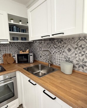 A modern kitchen with white cabinets, a stainless steel sink, a microwave, and a patterned backsplash. - Comfortable downtown apartment with a terrace (Villasimius)