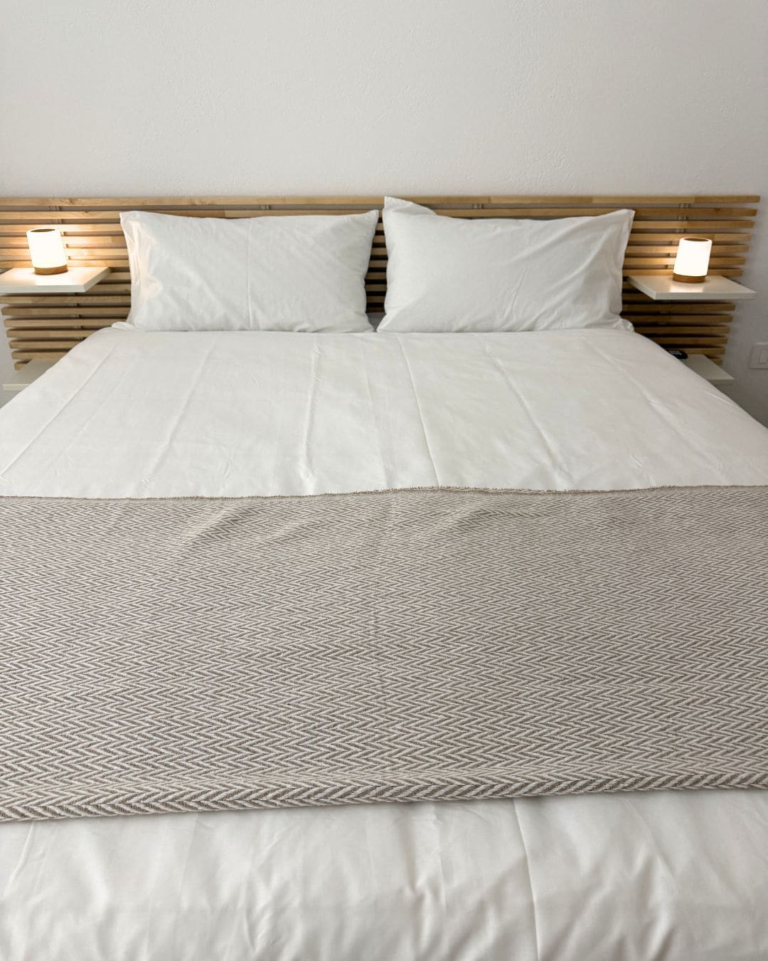 Un lit avec une tête de lit en bois, deux lampes de chevet et un tapis à motifs.