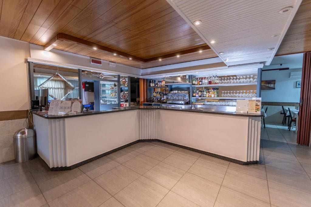 Uma área de bar com balcão curvo, prateleiras com garrafas e copos.