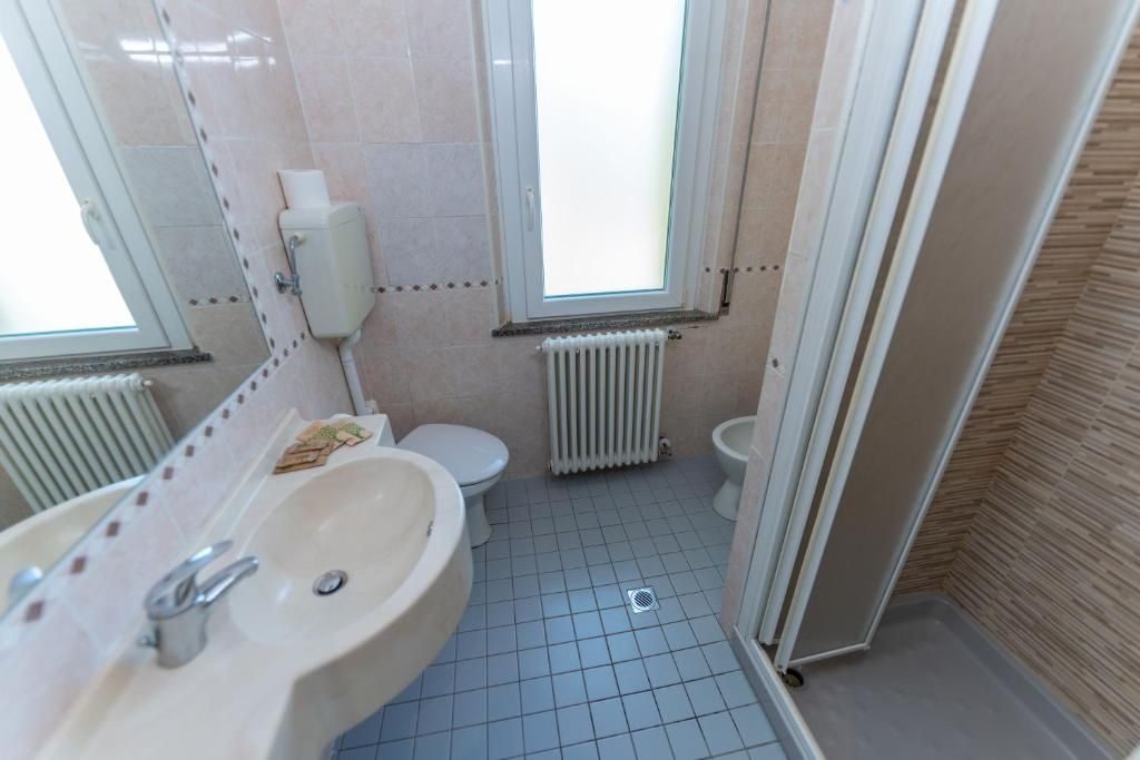 Un baño con lavamanos, dos inodoros, una ventana y un radiador.
