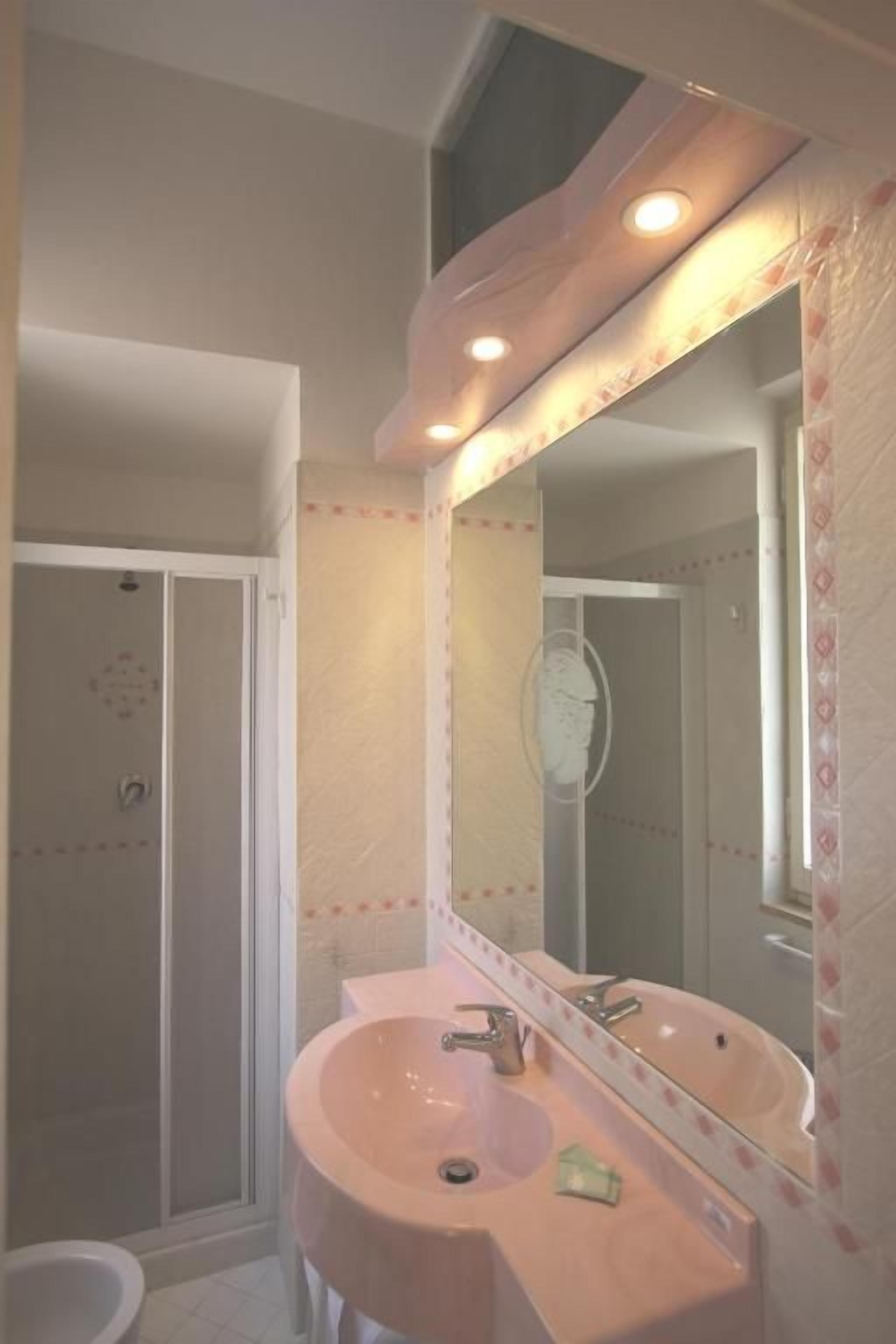 Casa de banho com uma pia rosa, espelho e porta de chuveiro.