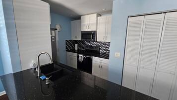 A compact kitchen with a black countertop, stainless steel appliances, and white cabinets.