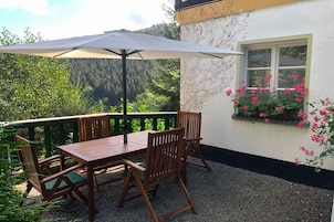 Un patio con una mesa, sillas, una sombrilla y vistas a un área boscosa.