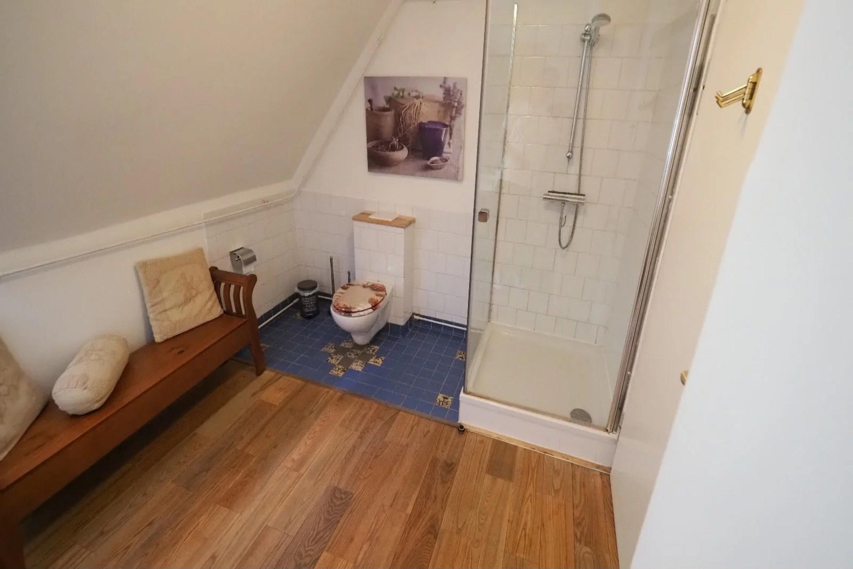A bathroom with a wooden bench, a toilet, a shower, and a tiled floor.