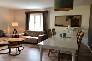 A modern living room with a sofa, two round tables, a dining table with chairs, a large window with curtains, a floor lamp, and a mirror on the wall.