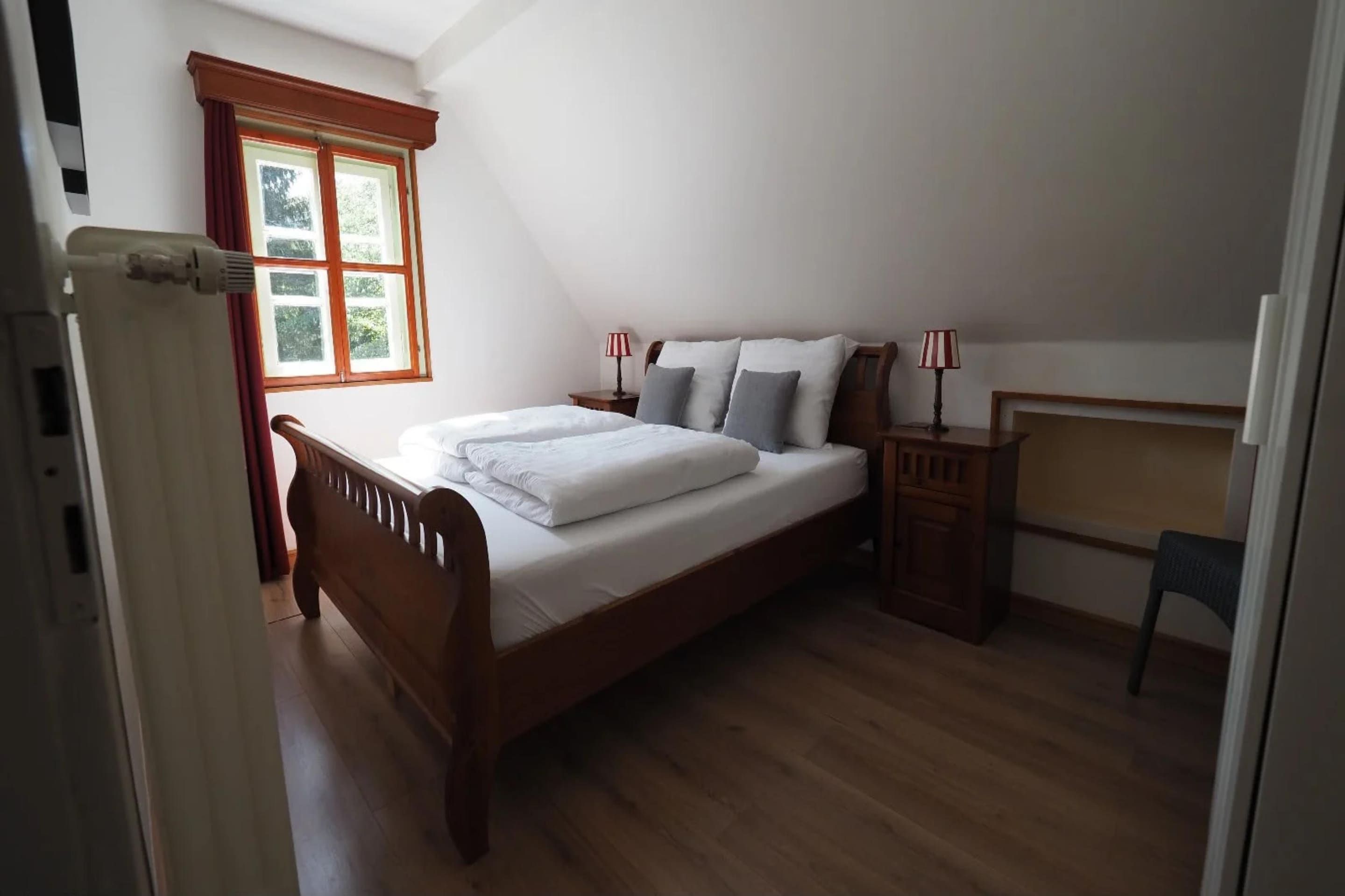 A bedroom with a wooden bed, a nightstand, a desk, and a window with curtains.