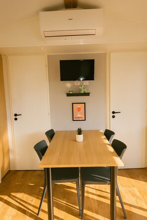 Quarto com mesa de madeira, quatro cadeiras, televisão na parede e aparelho de ar condicionado.