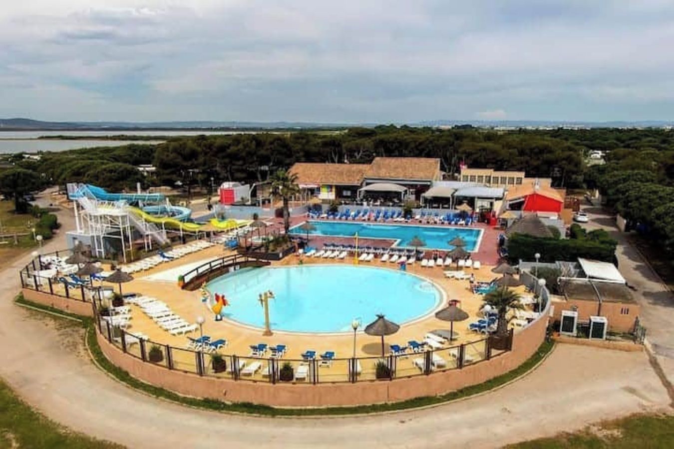 Une grande piscine avec un toboggan, entourée de chaises longues et de parasols, et offrant une vue sur la mer en arrière-plan.