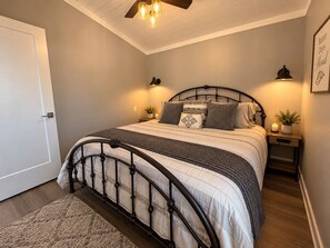 Ein Schlafzimmer mit einem Bett, Nachttischlampen, einem Nachttisch, einer Tür und einem Deckenventilator.