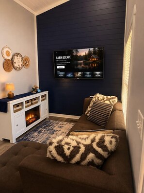 Ein Wohnzimmer mit Kamin, einem an der Wand montierten Fernseher und einem Sofa mit Kissen.