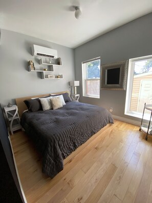 A bedroom with a bed, bedside tables, a wall-mounted air conditioner, a window with a view, and a ceiling fan. - Fully Furnished 1BR + Parking | Harbord Village | 5 months: $3800/month Oct–Mar (Toronto)