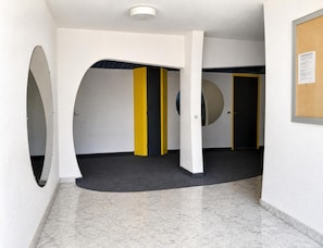 Um corredor com paredes brancas, piso de mármore e portas com detalhes em amarelo e preto.