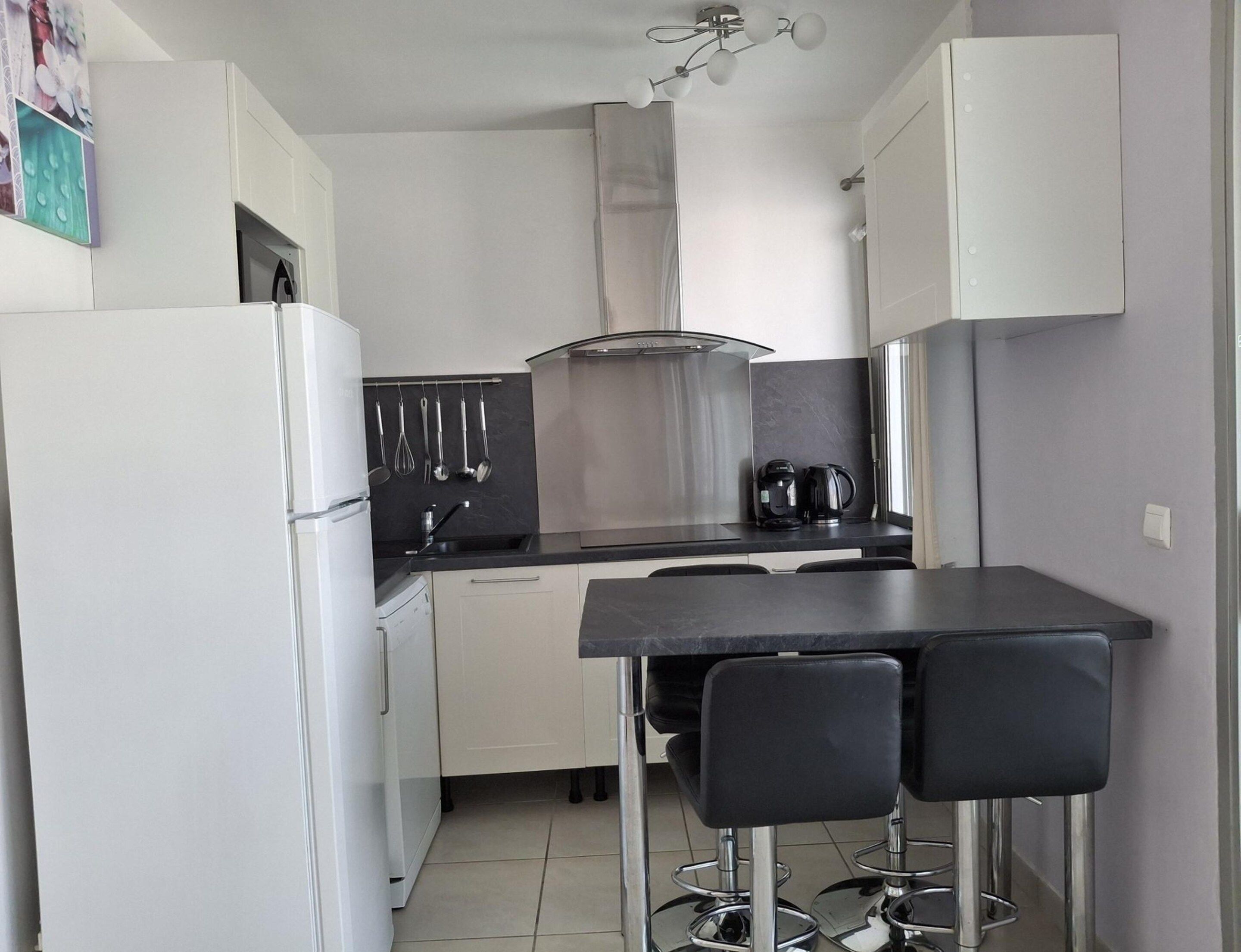 A compact kitchen with a refrigerator, stove, sink, and two bar stools.