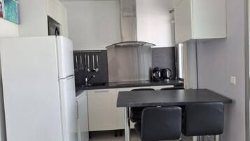 A compact kitchen with a refrigerator, stove, sink, and two bar stools.