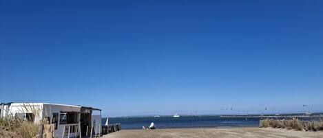 A beach with a wooden boardwalk, a small building, and a clear blue sky.