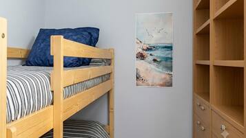 A bunk bed with striped bedding, a blue pillow, and a framed picture of a beach scene.