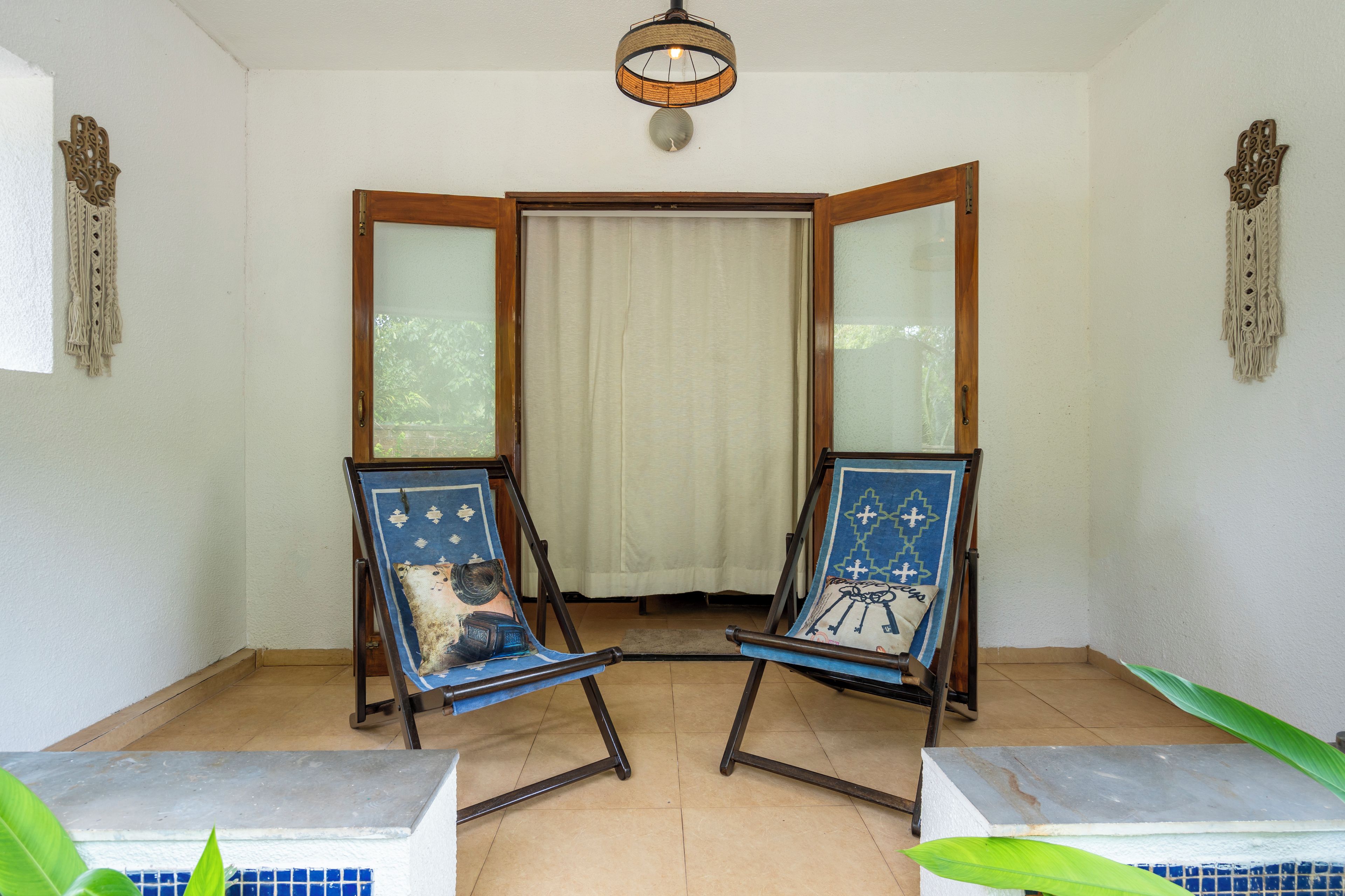 A room with two wooden-framed chairs with blue upholstery, a white curtain, and a ceiling light fixture.