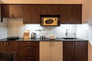 A compact kitchen with dark wooden cabinets, a built-in microwave, a kettle, a coffee maker, and a sink.
