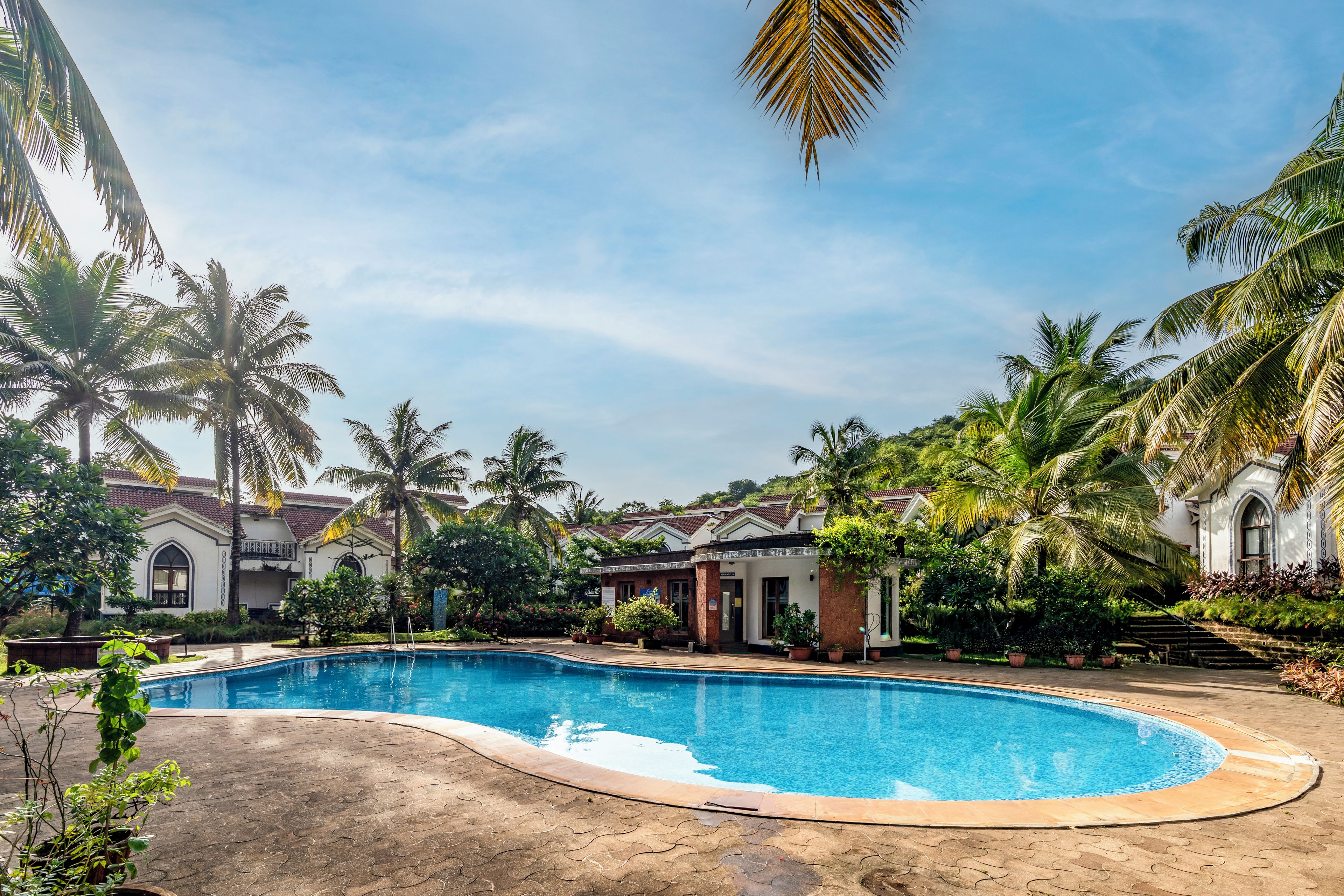 A swimming pool surrounded by palm trees and a building with a tiled roof.