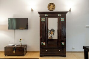 A dark wooden cabinet with decorative panels and a mirror, a television mounted on the wall, and a small table with a vase and a remote control. - Goan Hideaway - Earth (Arpora)