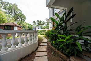 A pathway leading to a building with a white exterior and a balcony with a balustrade. - Goan Hideaway - Earth (Arpora)