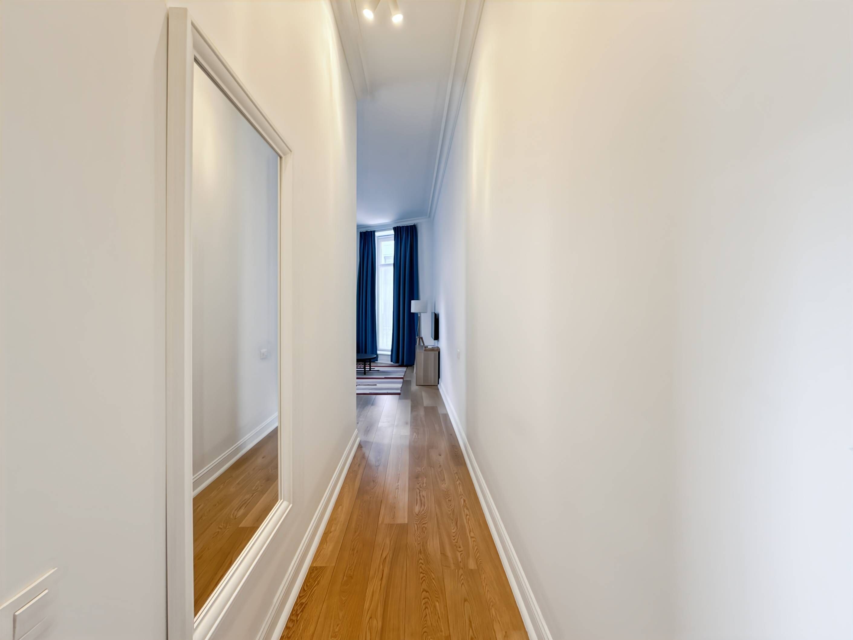 Un couloir étroit avec un plancher en bois et des murs blancs.