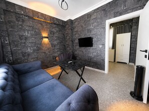 Een kamer met een donkere stenen muur, een flatscreen televisie boven een tafel en een bank.