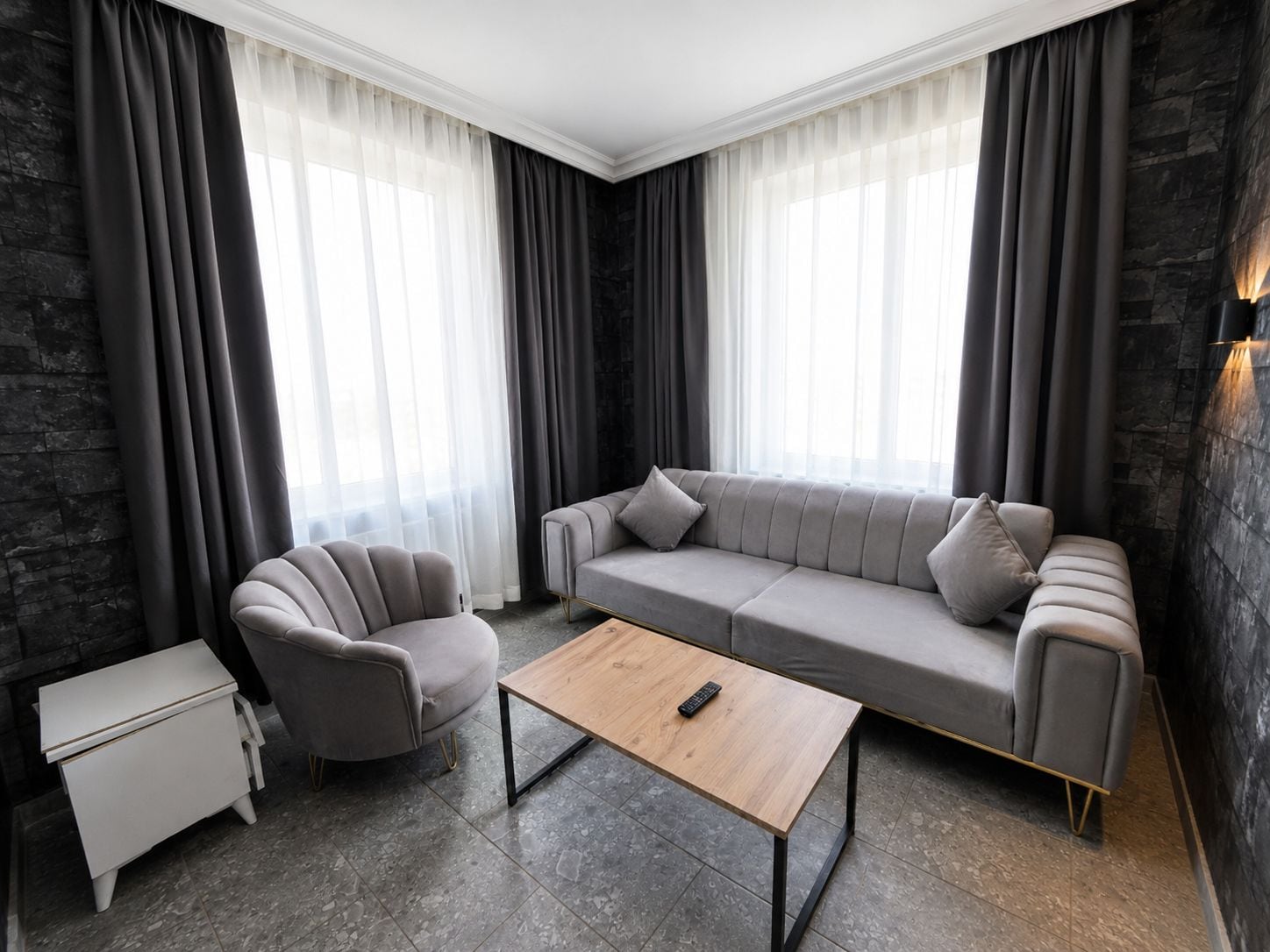 Un salon moderne avec un canapé gris, un fauteuil assorti, une table basse en bois et une petite table d’appoint blanche.