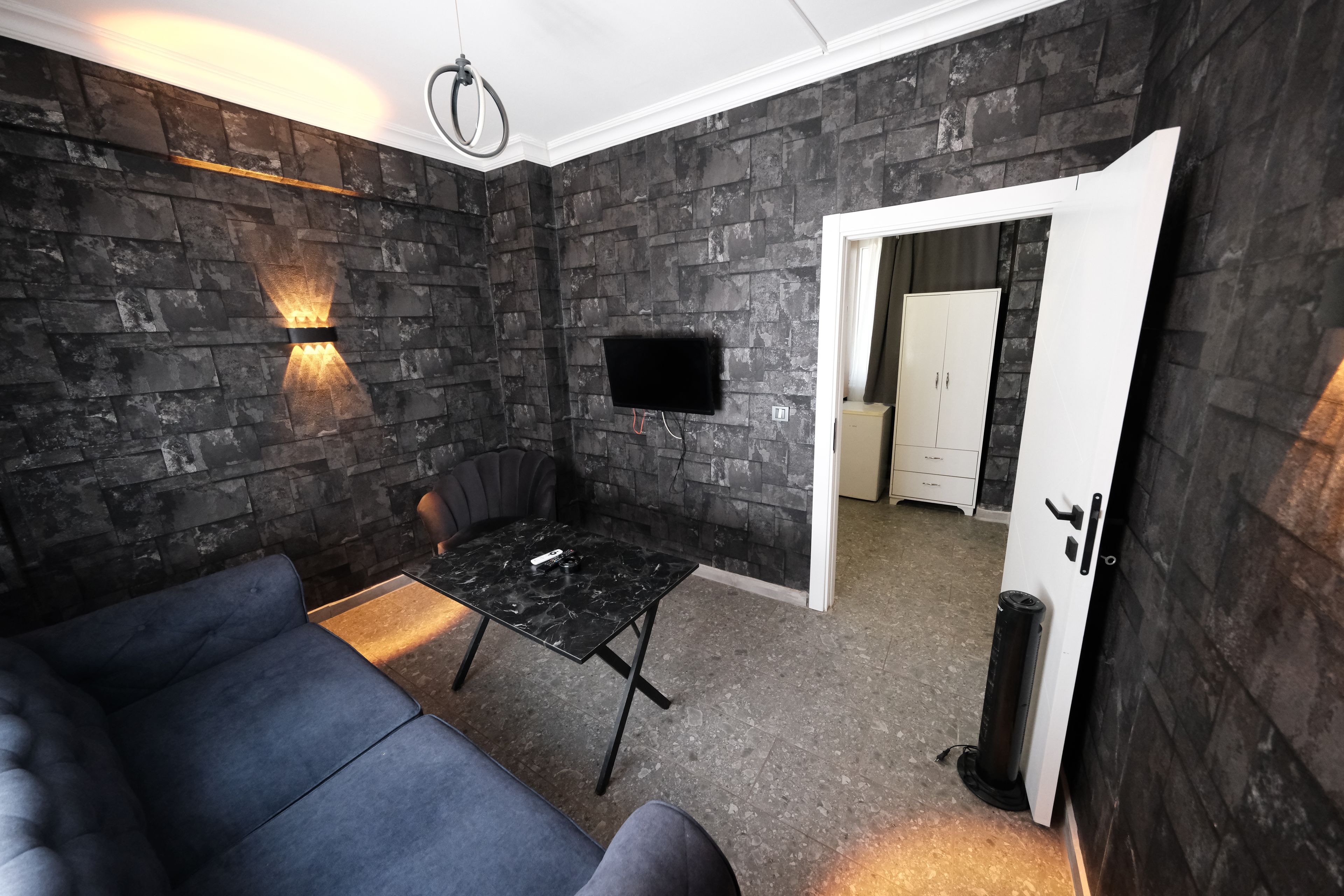 A modern room with a stone wall, a flat-screen TV mounted on the wall, a black leather sofa, and a small table with a remote control on it.