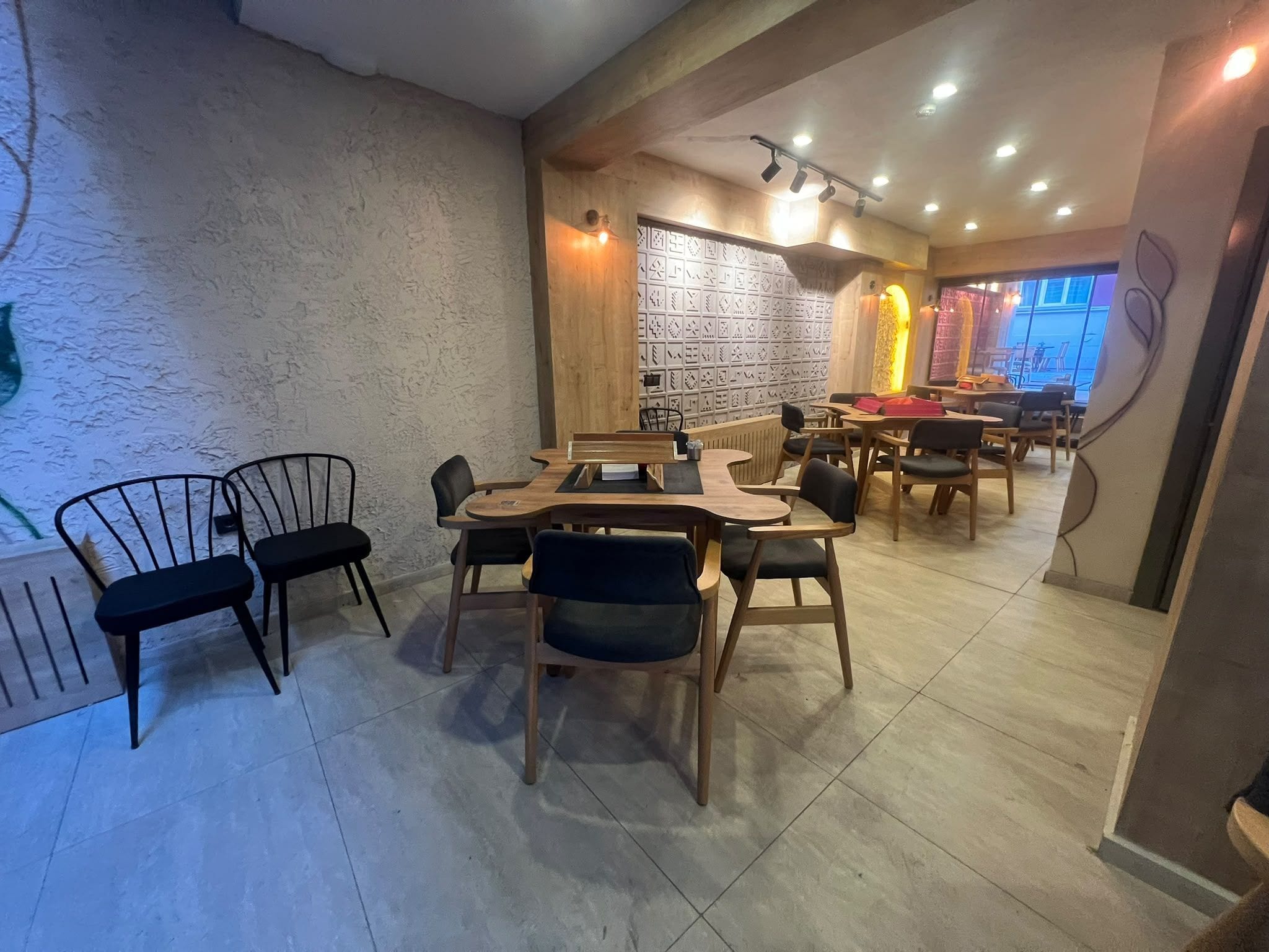 L’intérieur d’un restaurant avec des tables et des chaises en bois, un mur orné de motifs et un éclairage encastré au plafond.