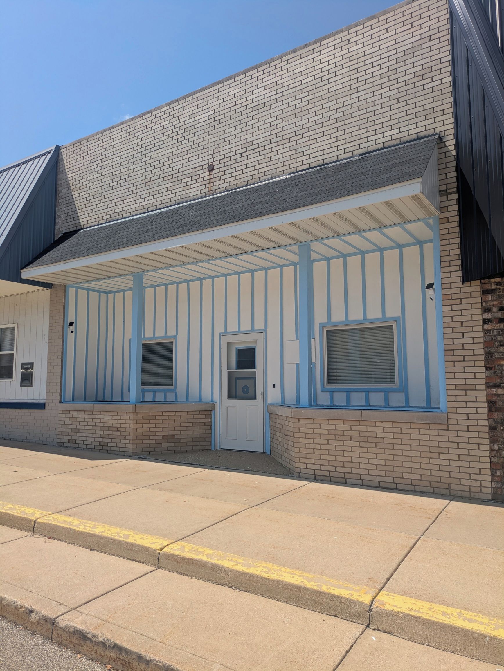 A building with a brick facade, a covered entrance with blue trim, and a door with a window.