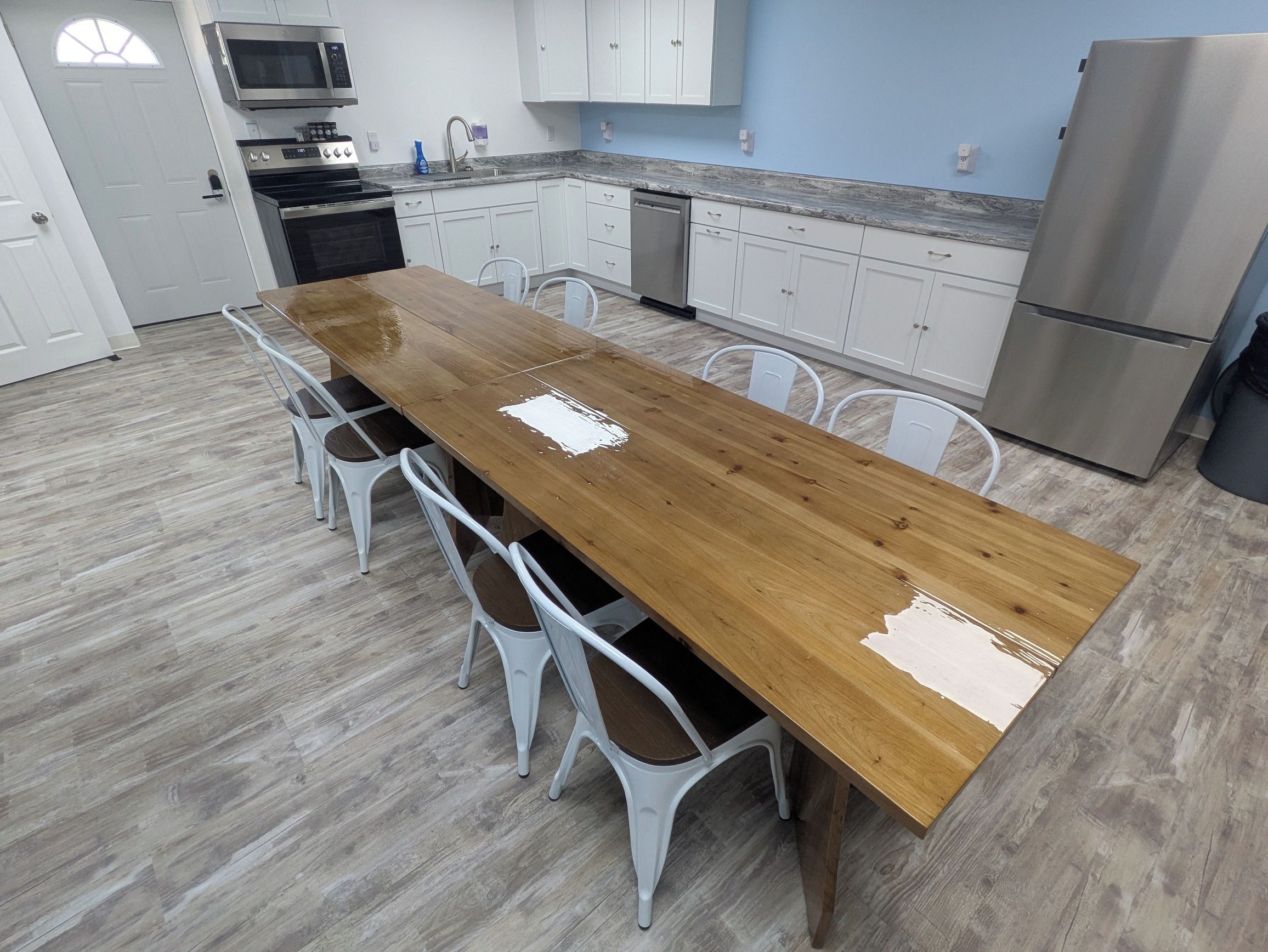 Een keuken met een houten eettafel, witte stoelen, een roestvrijstalen koelkast en witte kastjes.