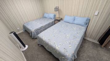 A hotel room with two beds, a bedside table, a lamp, and a wall-mounted light switch.