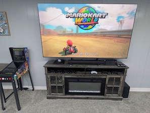 A television displaying Mario Kart World, with a gaming console and controllers on a wooden entertainment unit.