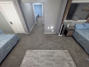 A bedroom with two beds, a bedside table, a lamp, and a hallway leading to another room.