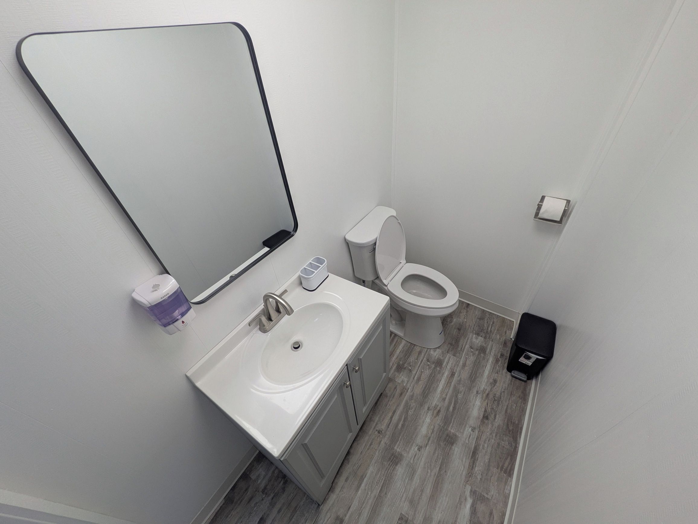 A bathroom with a white sink, mirror, toilet, and a trash bin.