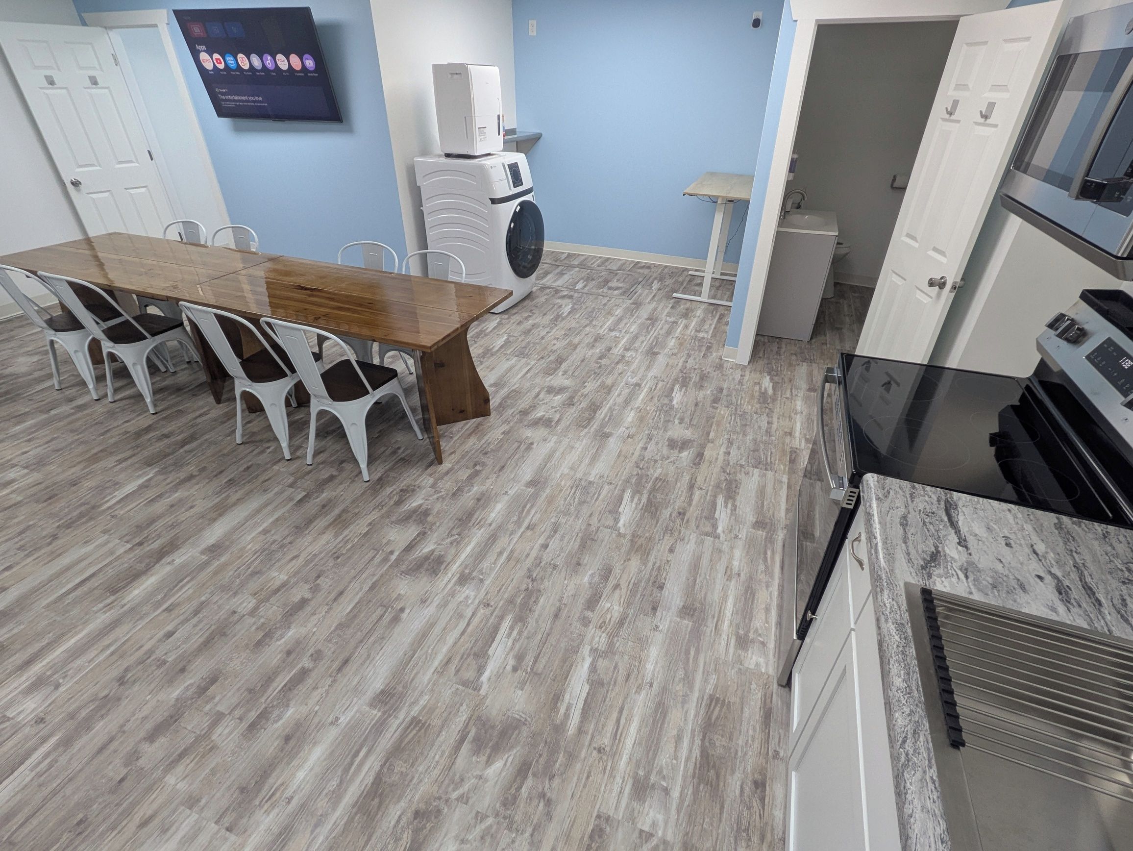 Een moderne keuken met een houten eettafel en stoelen, een inbouwoven en een aan de muur bevestigde televisie.