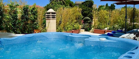 A hot tub surrounded by lush greenery and a castle-like structure in the background.
