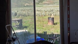 Ein Zimmer mit großem Fenster und Blick auf eine gebirgige Landschaft, ein rustikaler Holzsessel und ein Metallfass.