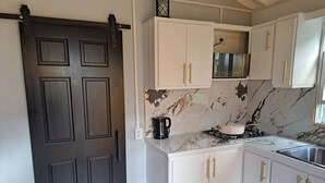 Una cocina con armarios blancos, una puerta negra, un lavamanos de acero inoxidable y una estufa a gas.
