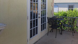 Un patio con una mesa y sillas, una puerta con paneles de vidrio y un farol colgante en la pared.