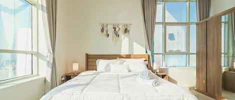 A hotel room with a large bed, two bedside tables, a wall-mounted decoration, and a view through the window.