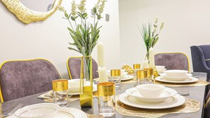 Een eettafel gedekt met witte borden, glazen met goudkleurige rand en een vaas met witte bloemen.