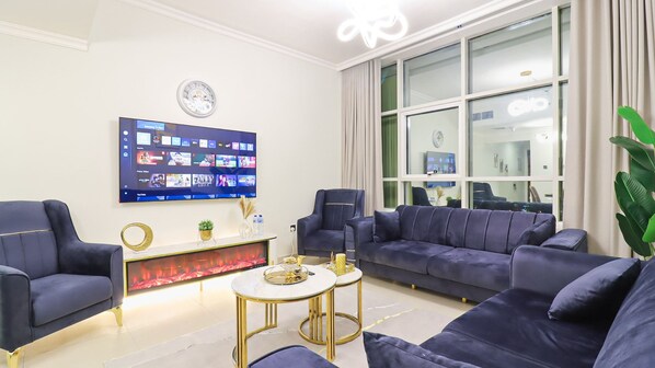 Een moderne woonkamer met een grote flatscreen televisie aan de muur, een zithoek en een klein bijzettafeltje.
