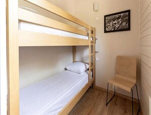 A bunk bed with a wooden frame, a single bed below, a chair, and a wall-mounted light fixture. - Mountain Apartment for 6 in Ax-les-thermes (Ax-les-Thermes)