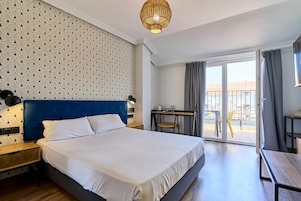 Habitación de hotel con una cama grande, un escritorio, una silla y un balcón con vistas.