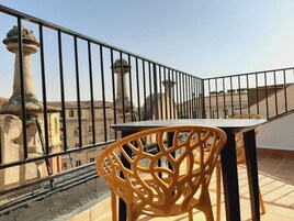 A balcony with a table and chairs, overlooking a cityscape with buildings and a tower.