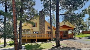 Une maison à deux étages avec une cheminée en pierre, une terrasse en bois et un porche couvert.